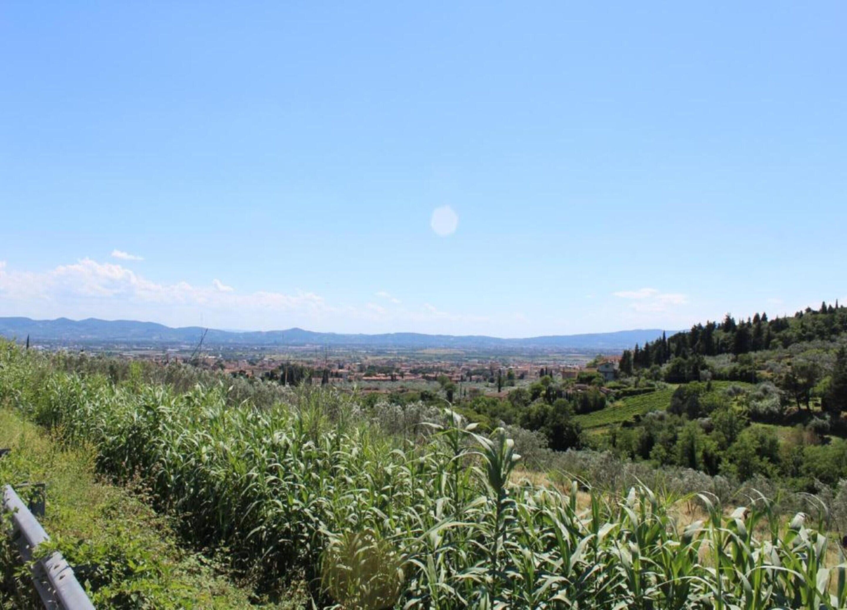 A panoramic view of a landscape with a distant town, rolling hills, and a clear sky.