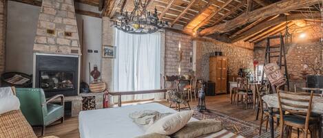 A rustic room with a stone fireplace, wooden beams, a chandelier, and a dining area.