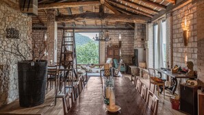 A rustic dining area with a long wooden table, chairs, and a view of a mountainous landscape through a large window. - Belvilla by Oyo Casa Marchi (Vergato)