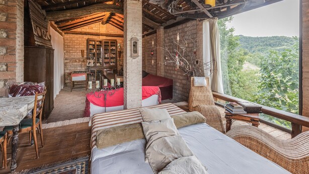 A rustic room with a bed, a wooden table, and a view of the forest. - Belvilla by Oyo Casa Marchi (Vergato)