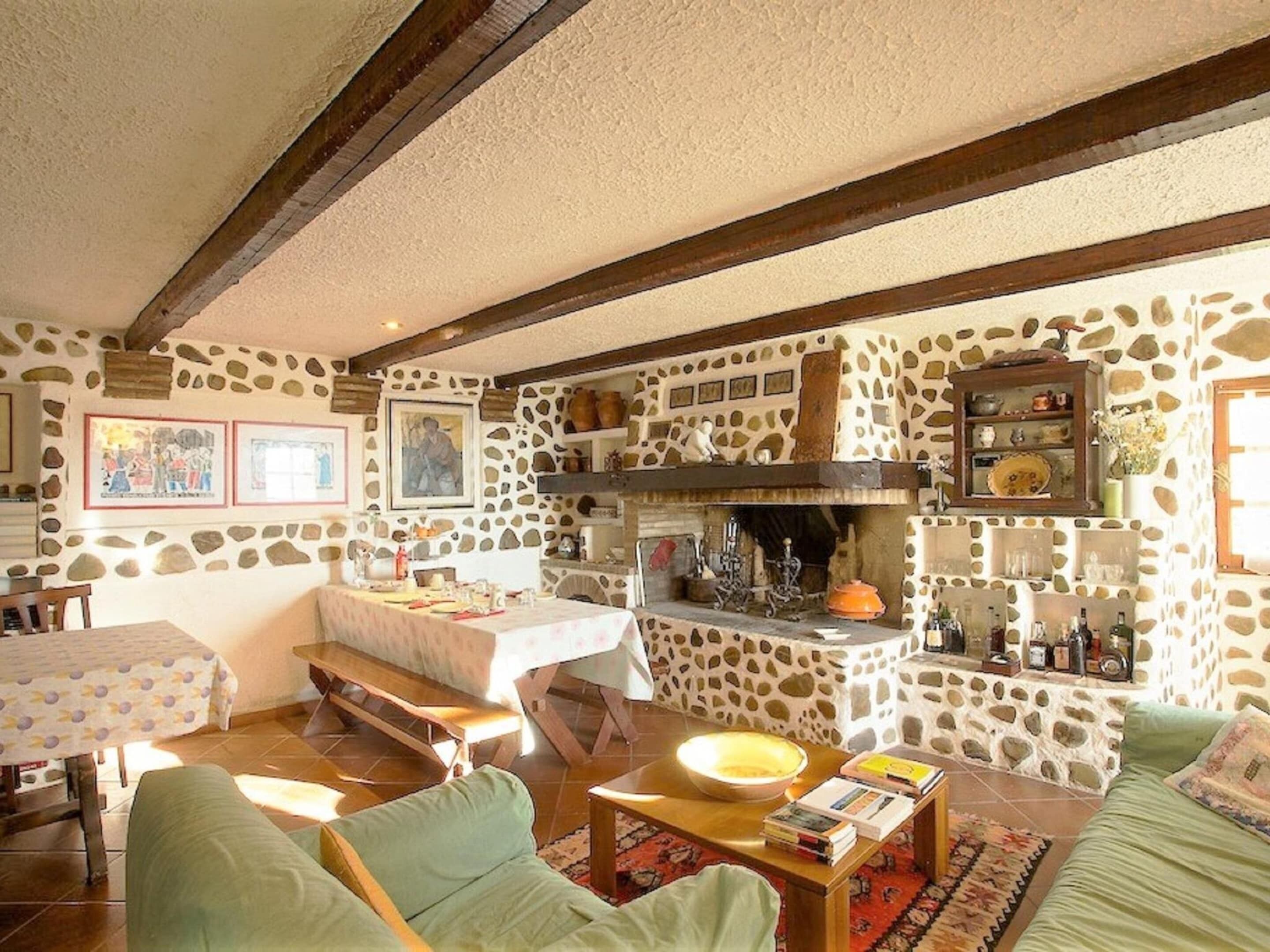 A rustic interior with a stone wall, wooden beams, a dining area, and a cozy seating area.