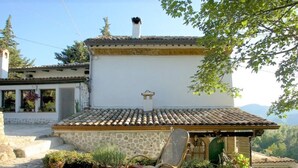Una construcción rústica con techo de tejas, paredes de piedra y un pequeño porche con una silla.