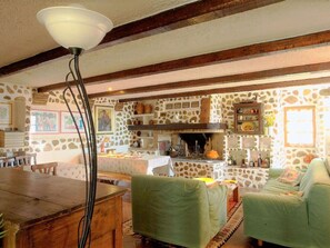 Un interno rustico con parete in pietra, travi in legno, zona pranzo e divano verde.