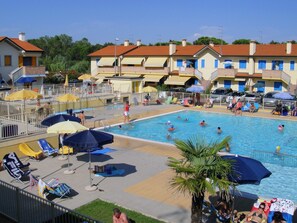 A swimming pool area with multiple sun loungers, umbrellas, and a poolside deck. - Belvilla by OYO Trilo 4 Solmare a Rosolina (Rosolina)