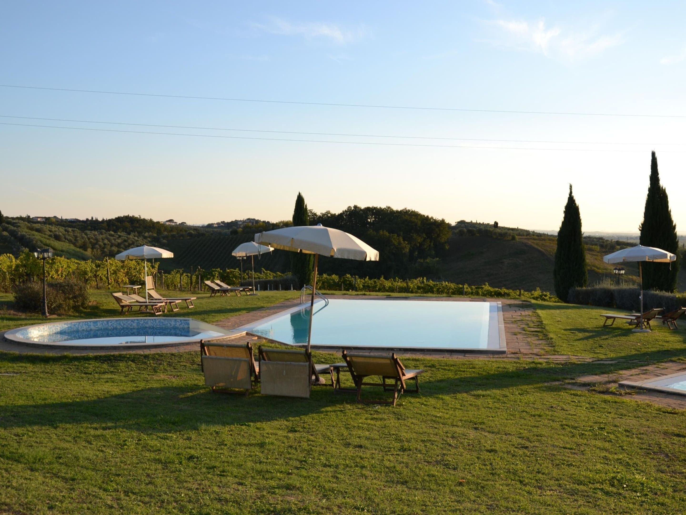 A pool area with lounge chairs and umbrellas, surrounded by grass and trees.