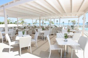 Ein Außenbereich mit Sitzgelegenheiten, weißen Korbmöbeln und Sonnenschirmen, mit Blick auf einen Pool und Strand.
