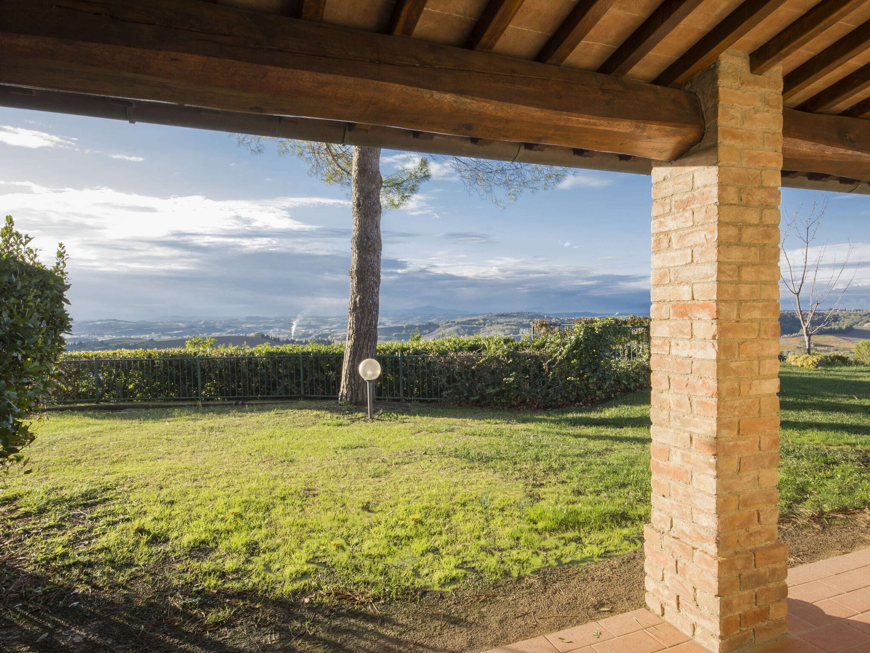 A covered outdoor area with a brick column, a metal fence, and a view of a vineyard and distant hills.