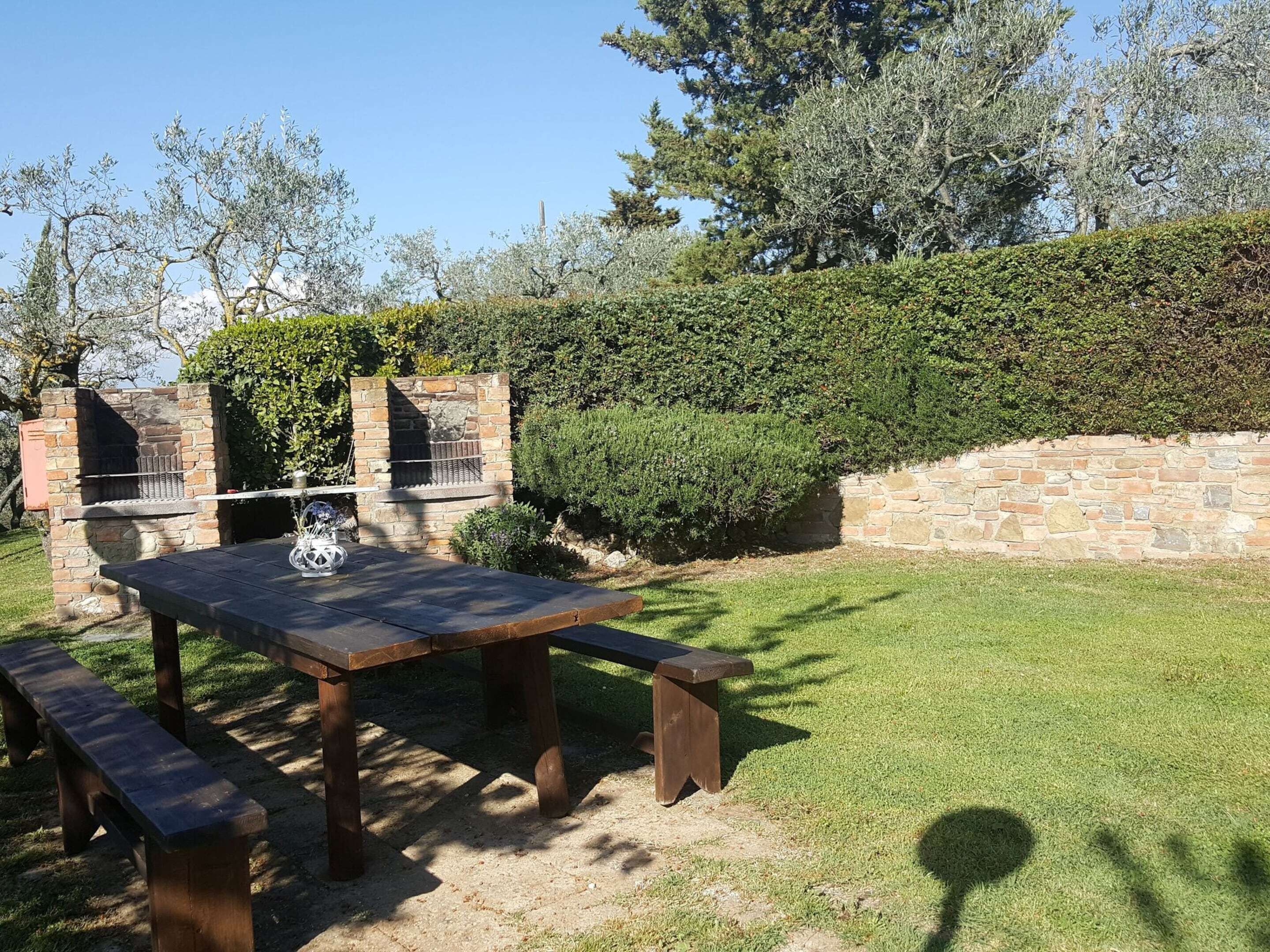 An outdoor patio with a stone barbecue grill, a wooden table, and benches.