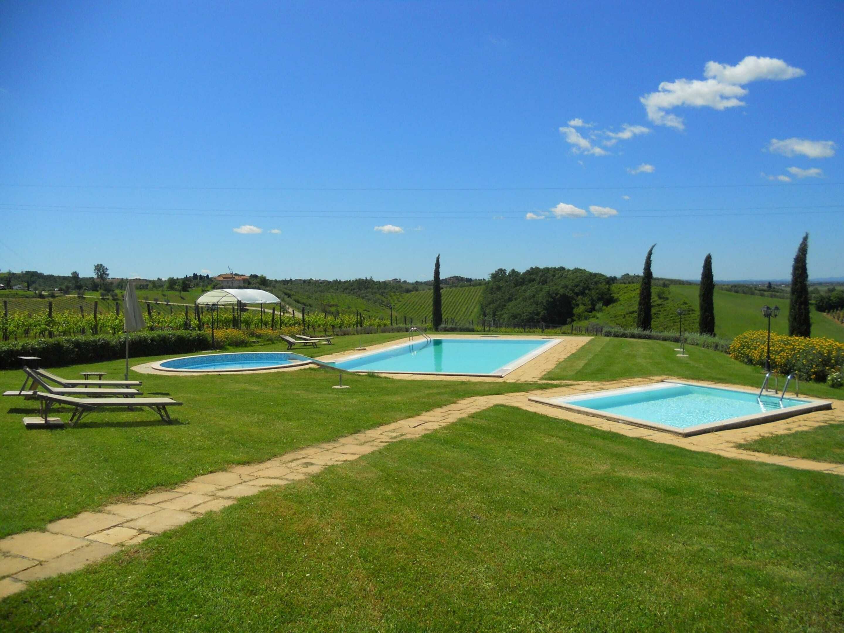 Zona de piscina con dos piscinas rectangulares, una pérgola y sillones de descanso.