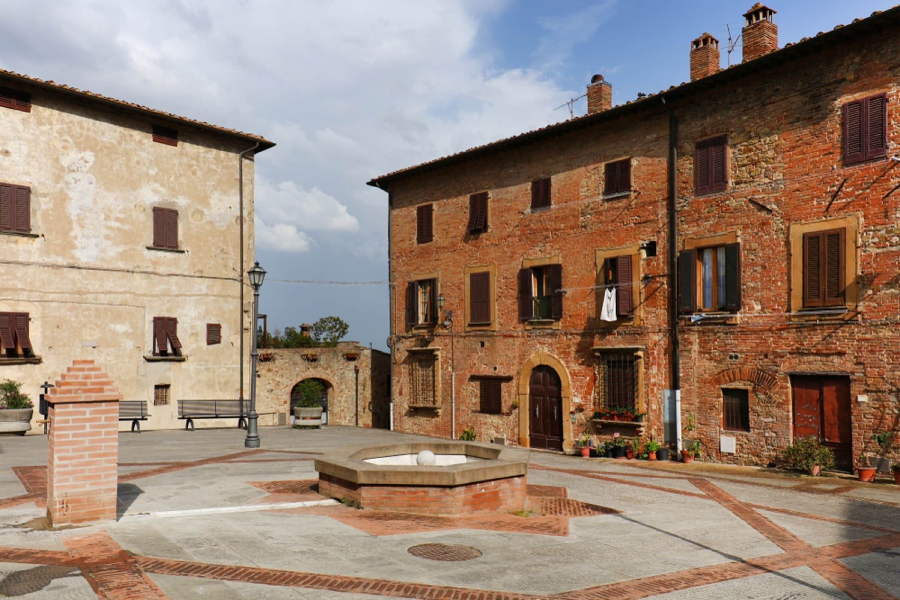 A courtyard with a fountain, surrounded by historic buildings with brick facades and arched doorways.