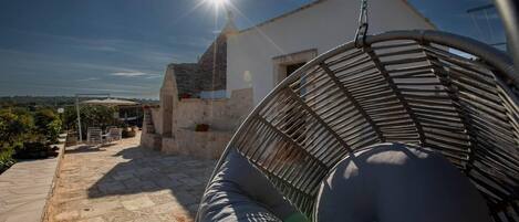 A stone patio with a hanging chair and a white building in the background.