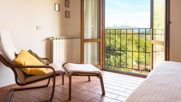 A balcony with a view of greenery and mountains, a chair with a cushion, and a bed with a white duvet. - Holiday Home in Vicchio With Private Pool (Vicchio)