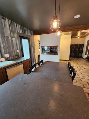 A modern kitchen with a large island, dark countertops, and a hanging light fixture.