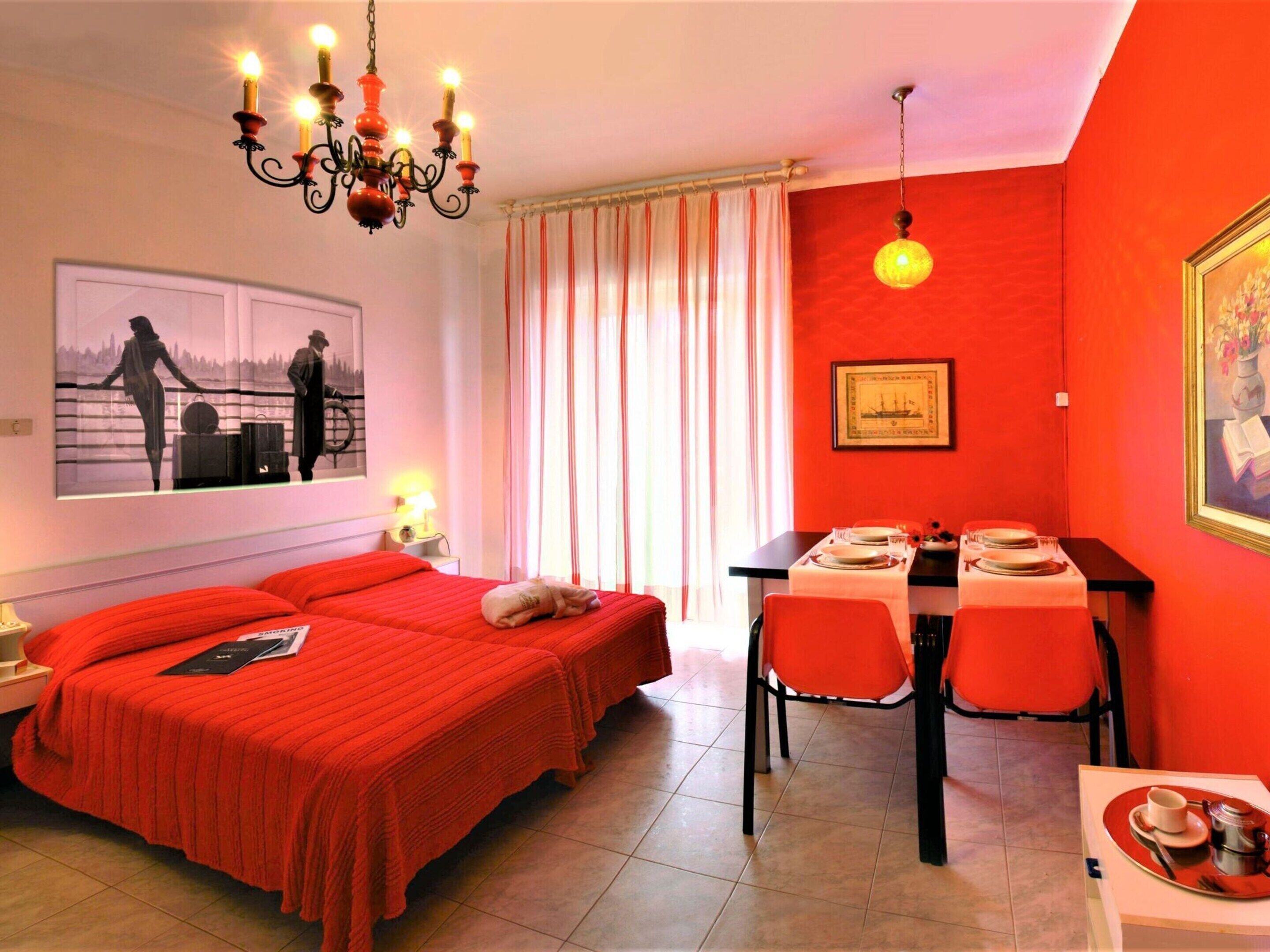 A hotel room with two beds, a dining table with chairs, a chandelier, and artwork on the walls.