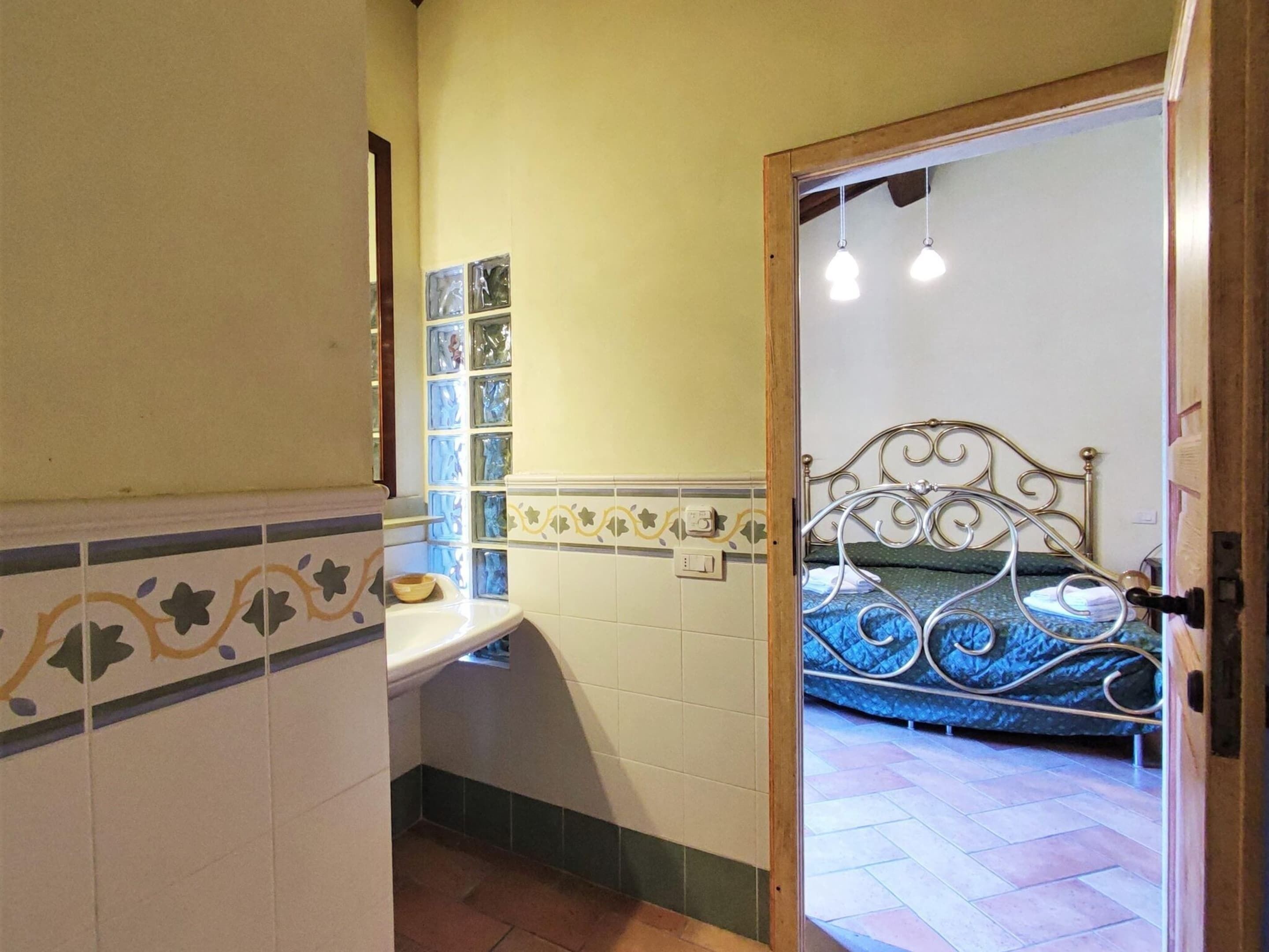 Een slaapkamer met een bed met metalen frame, een nachtkastje en een raam met decoratieve glasblokken.