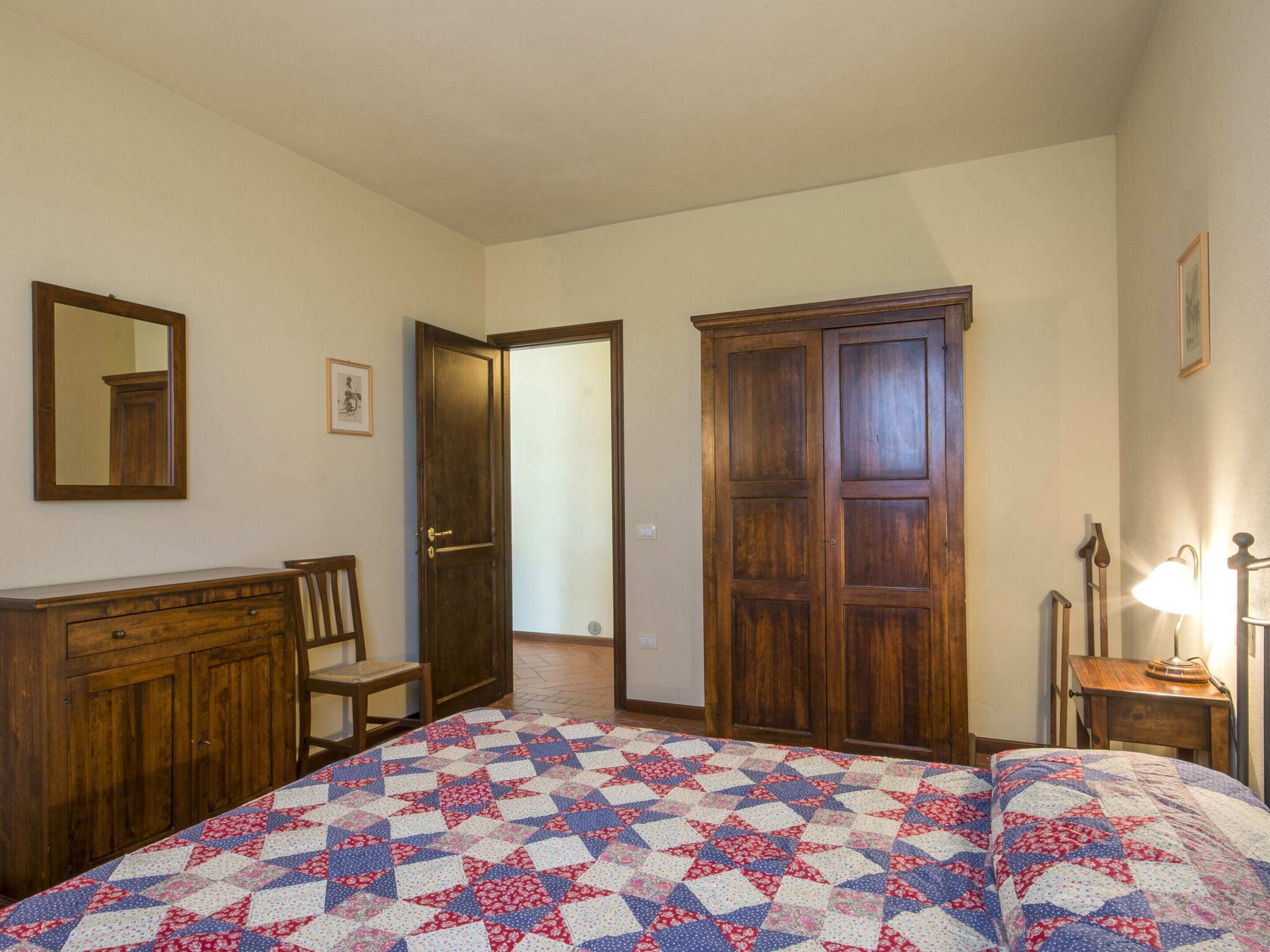 A bedroom with a bed, a dresser, a chair, a wardrobe, and a mirror.