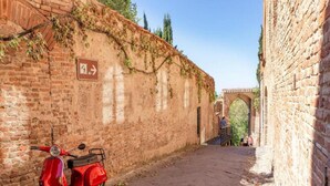 A narrow cobblestone street flanked by brick walls, a red scooter parked on the left, and an archway in the distance. - Countryside Home With Private Terrace (Castelfiorentino)