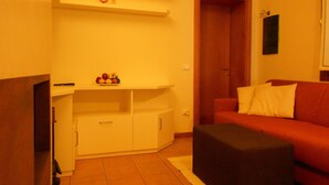 Un espacio habitable compacto con kitchenette, un sofá rojo y una pequeña mesa con fruta.