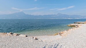 A pebbled beach with clear water and distant mountains. - Belvilla by OYO Gianni A Due Piao Due (Torri del Benaco)