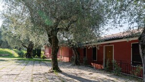 A red building with a stone-paved courtyard and a large tree in the center. - Belvilla by OYO Gianni A Due Piao Due (Torri del Benaco)