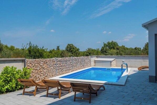 Relax by the pool surrounded by lush greenery and comfortable lounge chairs.