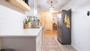 A modern kitchen with white cabinetry, a stainless steel refrigerator, and a hanging light fixture. - Designer Oasis: King Bed | Tranquil Backyard (Corpus Christi)