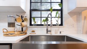 A modern kitchen with a stainless steel sink, a coffee maker, and a window with plants. - Designer Oasis: King Bed | Tranquil Backyard (Corpus Christi)