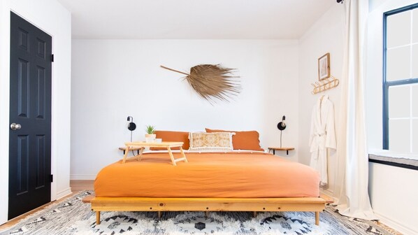 A bedroom with a bed, bedside tables, a wall-mounted lamp, a door, and a window. - Designer Oasis: King Bed | Tranquil Backyard (Corpus Christi)