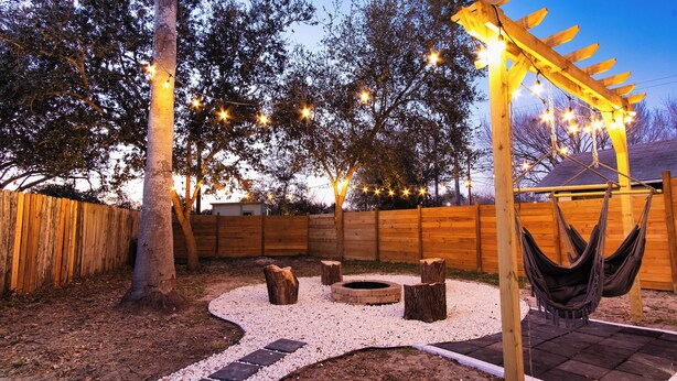 A backyard with a wooden pergola, hammock, fire pit, and string lights. - Designer Oasis: King Bed | Tranquil Backyard (Corpus Christi)