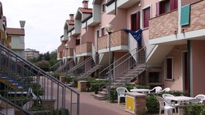 Una hilera de edificios de varios pisos con balcones, mesas al aire libre y una escalera que sube a los pisos superiores.