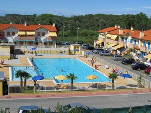 A swimming pool surrounded by buildings with balconies, a fenced area, and parked cars. - Belvilla by OYO Quadrilocale Solmare a Rosolina (Rosolina)