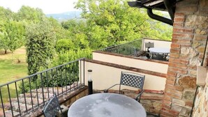 A balcony with a round table and two chairs, a brick wall, and a view of a green landscape. - Holiday Home in Gambassi Terme With Terrace (Gambassi Terme)