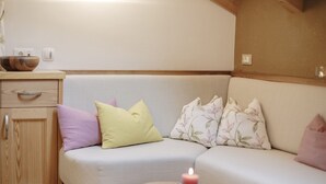 A cozy room with a sofa, pillows, a small table with a candle, and a wooden cabinet.