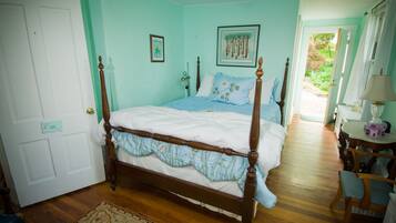 Quarto com cama de dossel, piso de madeira, porta com placa e pequena mesa com abajur.