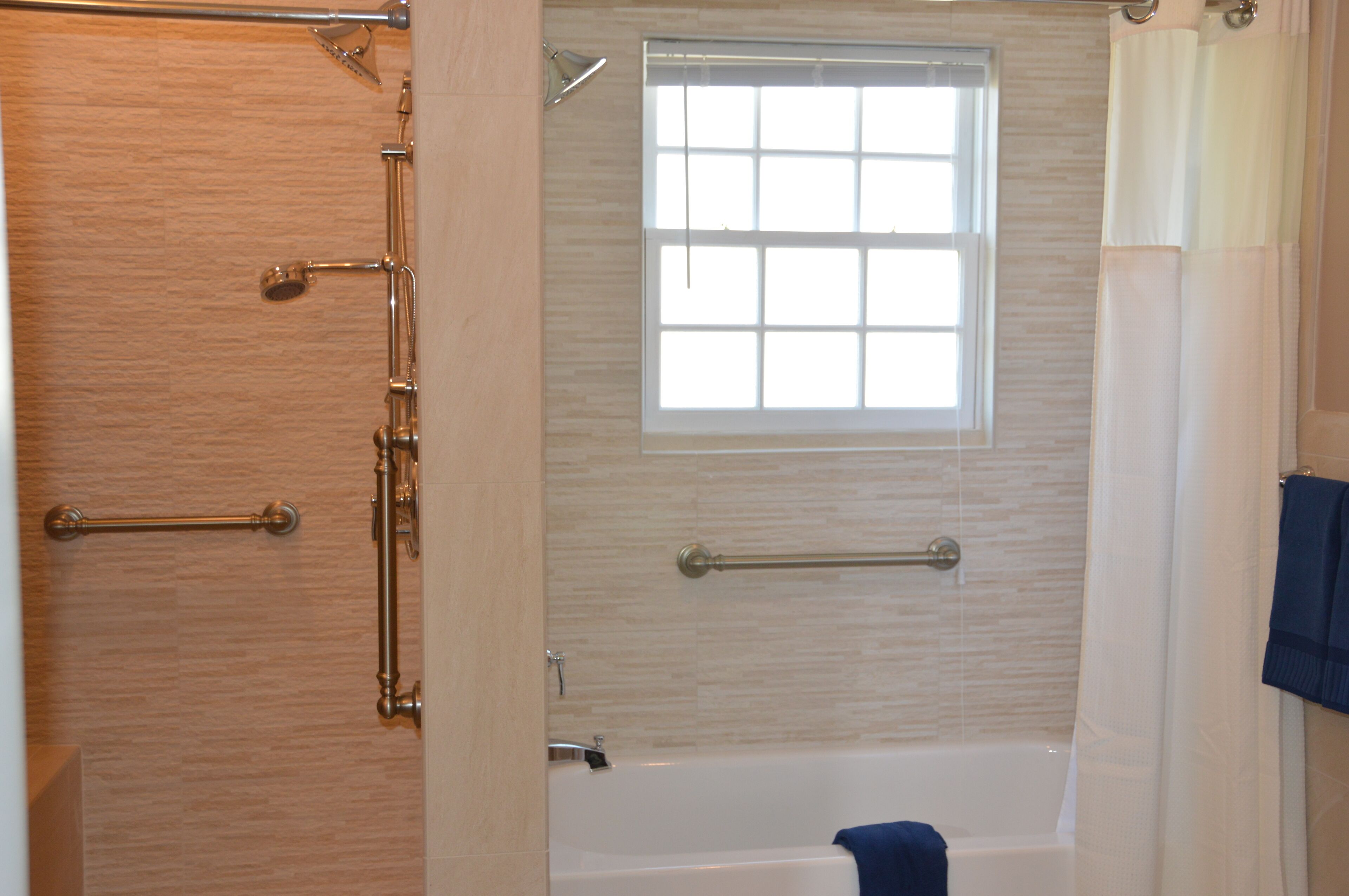 Bagno con vasca, una finestra e maniglie di sostegno.