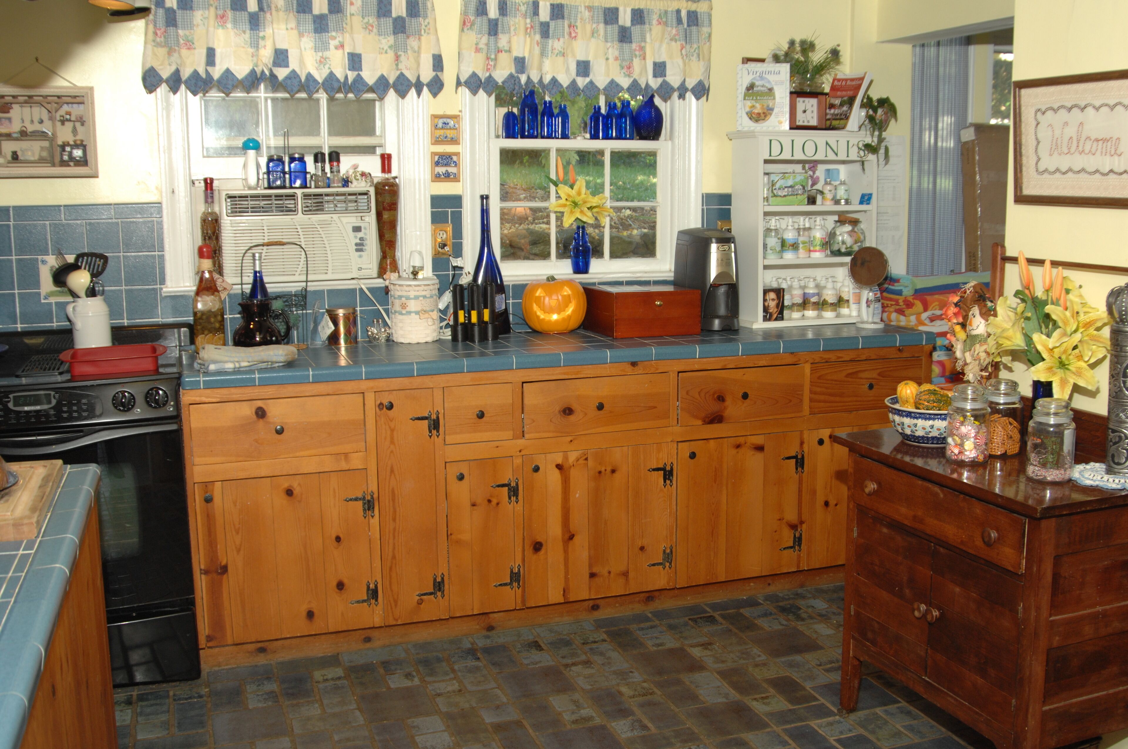 Una cocina con armarios de madera, estufa y ventana con cortinas azules.
