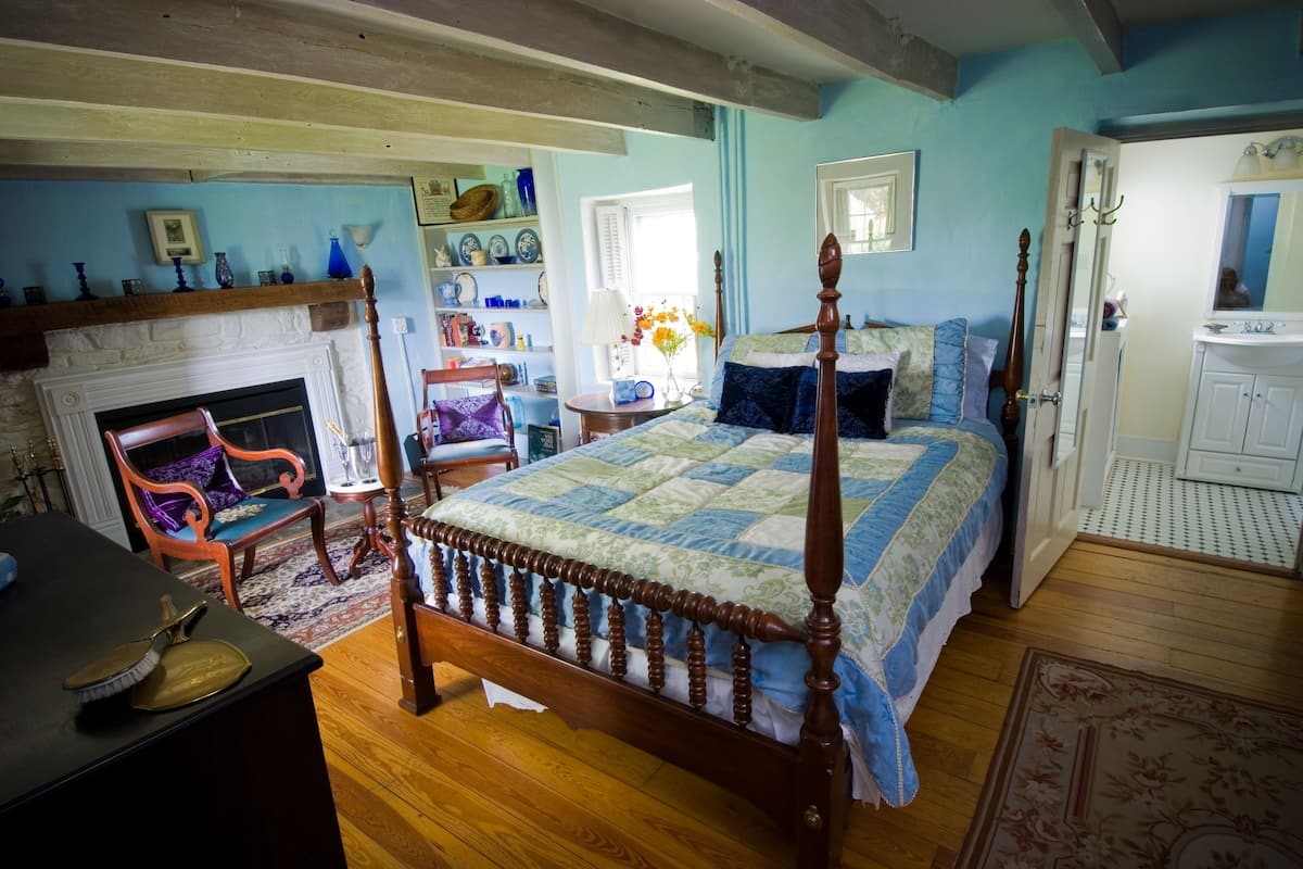 Quarto com cama de dossel, lareira, piso de madeira e banheiro com pia e espelho.