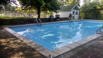 A rectangular swimming pool with a stone border, a small gazebo, and a grill area in the background.
