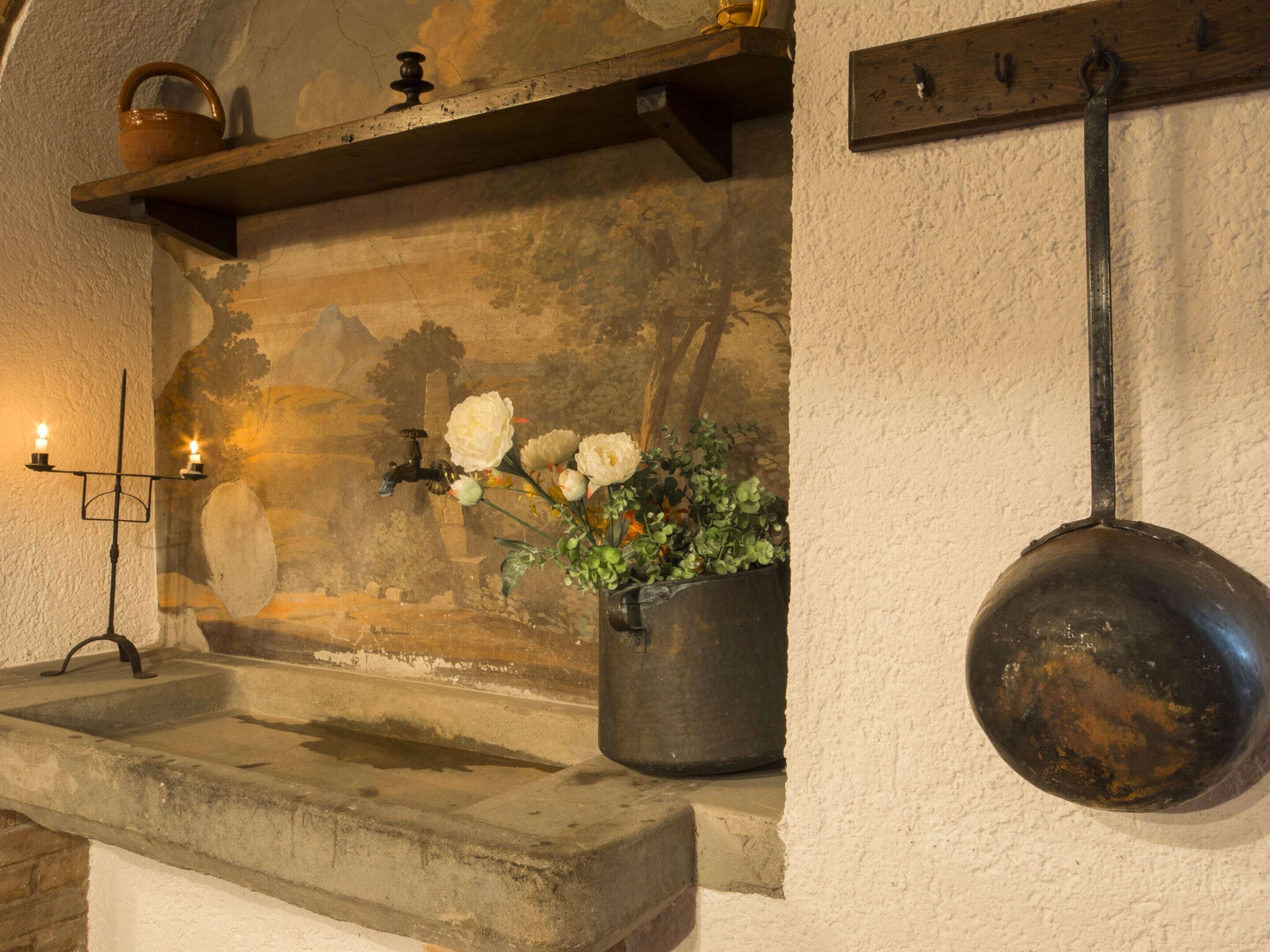A rustic kitchen with a stone sink, a hanging pot rack, and a potted plant with white flowers.