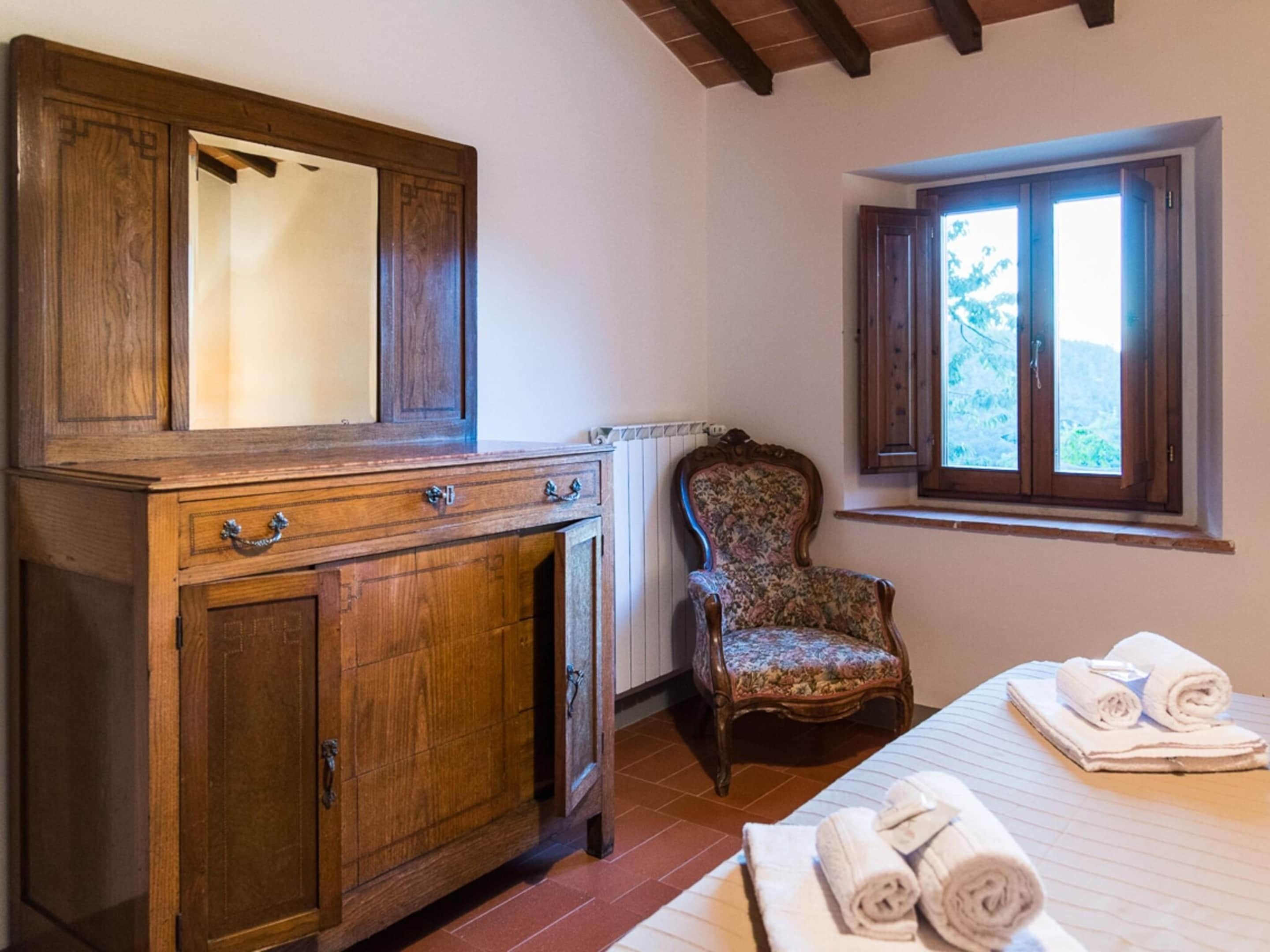 Une pièce avec un meuble en bois, une chaise, un lit avec des serviettes et une fenêtre avec des volets.