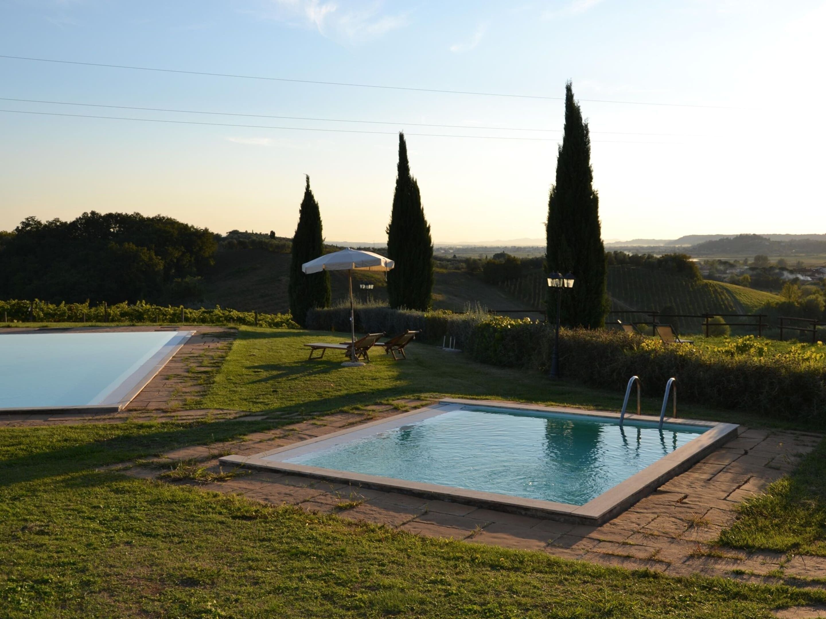 A swimming pool with two sun loungers and a small gazebo in a landscaped garden.