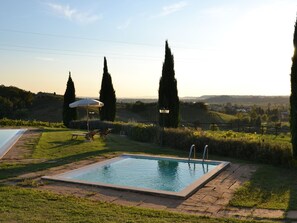 A rectangular pool with a tiled edge, surrounded by grass and a paved walkway. There are two lounge chairs and a white umbrella in the background. - Belvilla by OYO Primula (Cerreto Guidi)