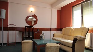 Una habitación con un sofá, una mesa, una silla, un taburete pequeño, un radiador, una lámpara y un espejo en la pared.