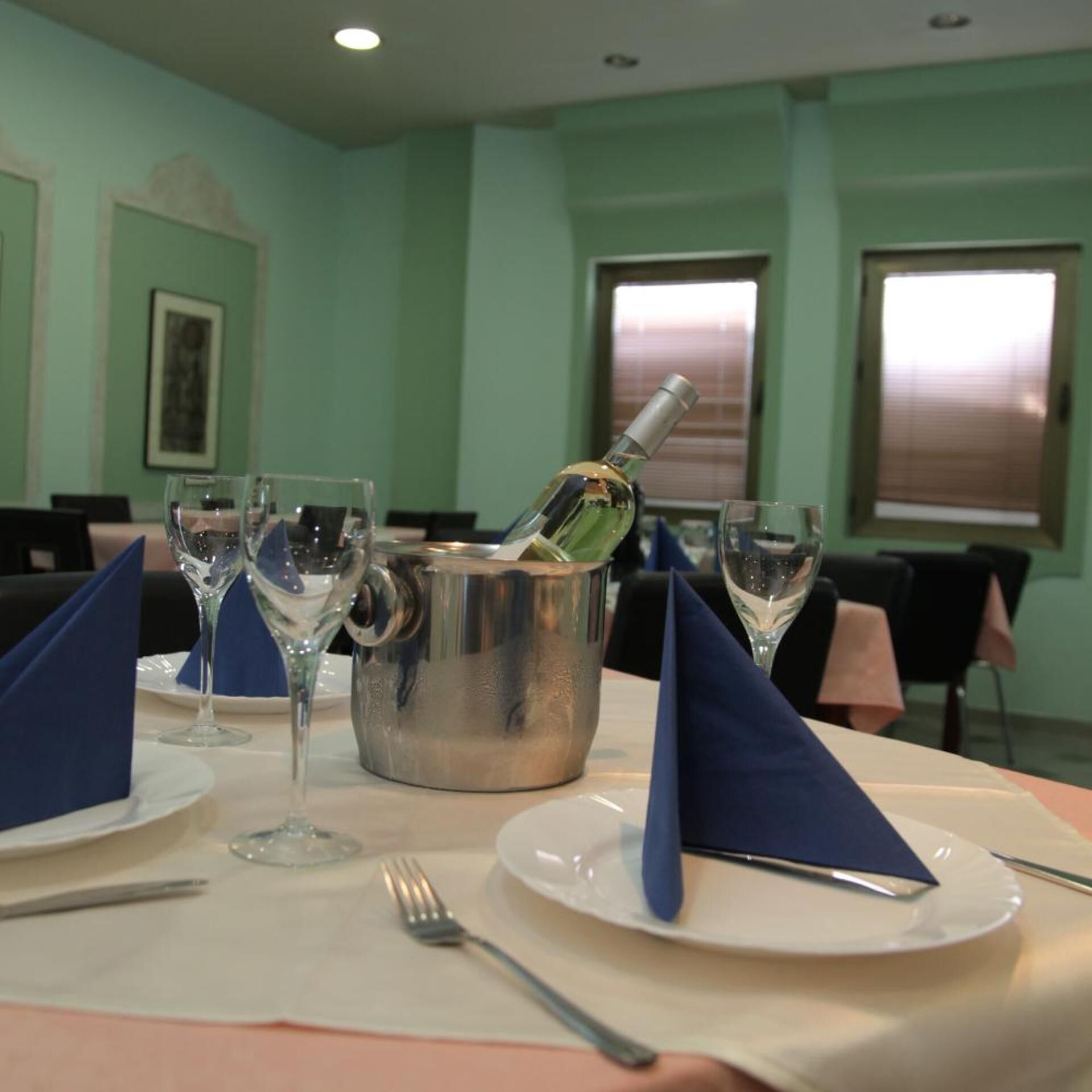 A dining table set with a bottle of champagne, wine glasses, and blue napkins.