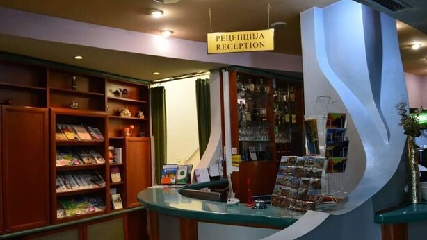 Un área de recepción con mostrador, una estantería con revistas y un letrero que indica la recepción.