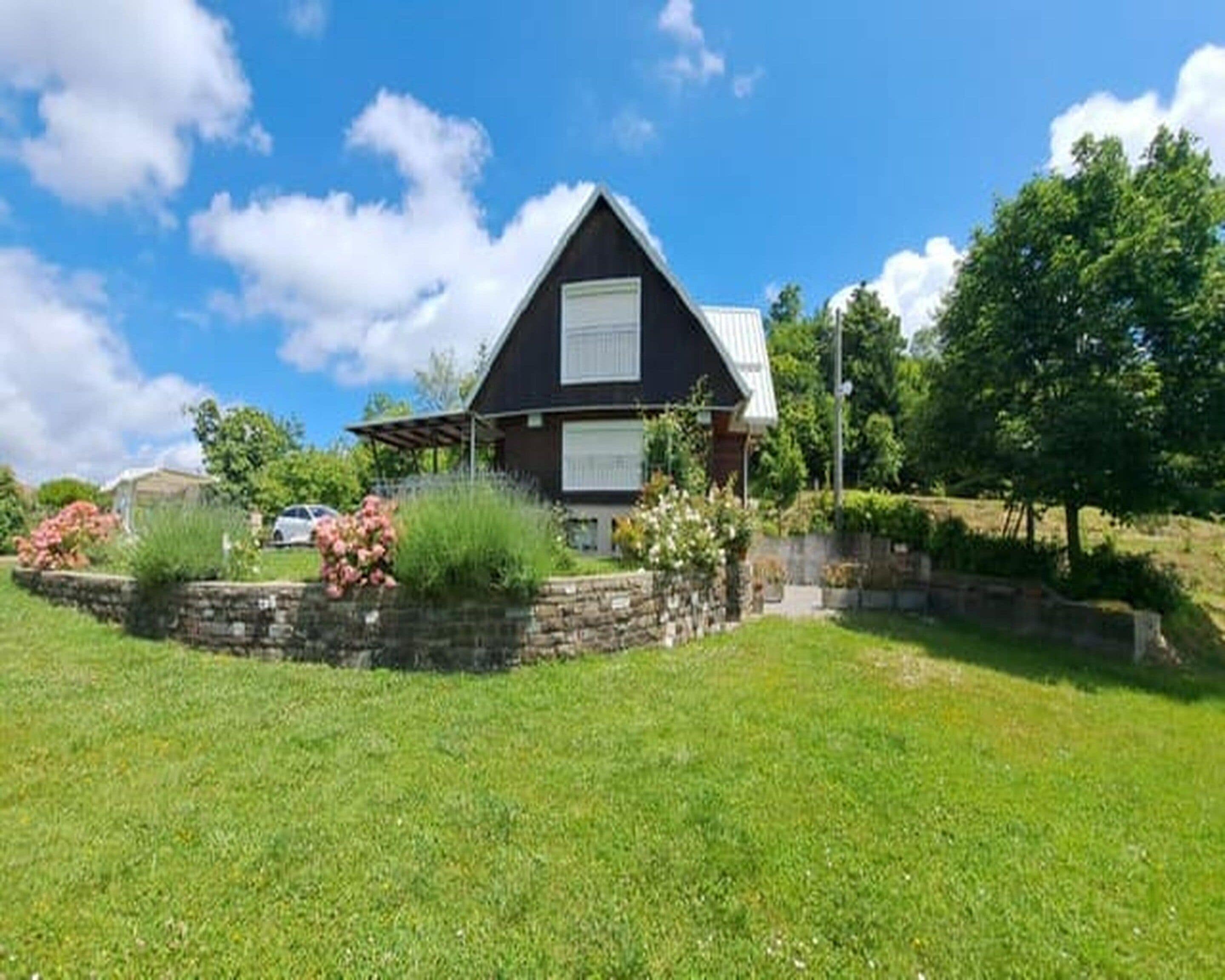 A house with a sloped roof, a front porch, and a stone retaining wall with plants.