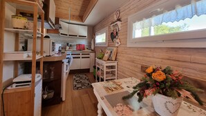 A cozy kitchen with wooden walls, a window with lace curtains, and a table with a floral centerpiece. - Chalet in Marliana Near Center (Marliana)