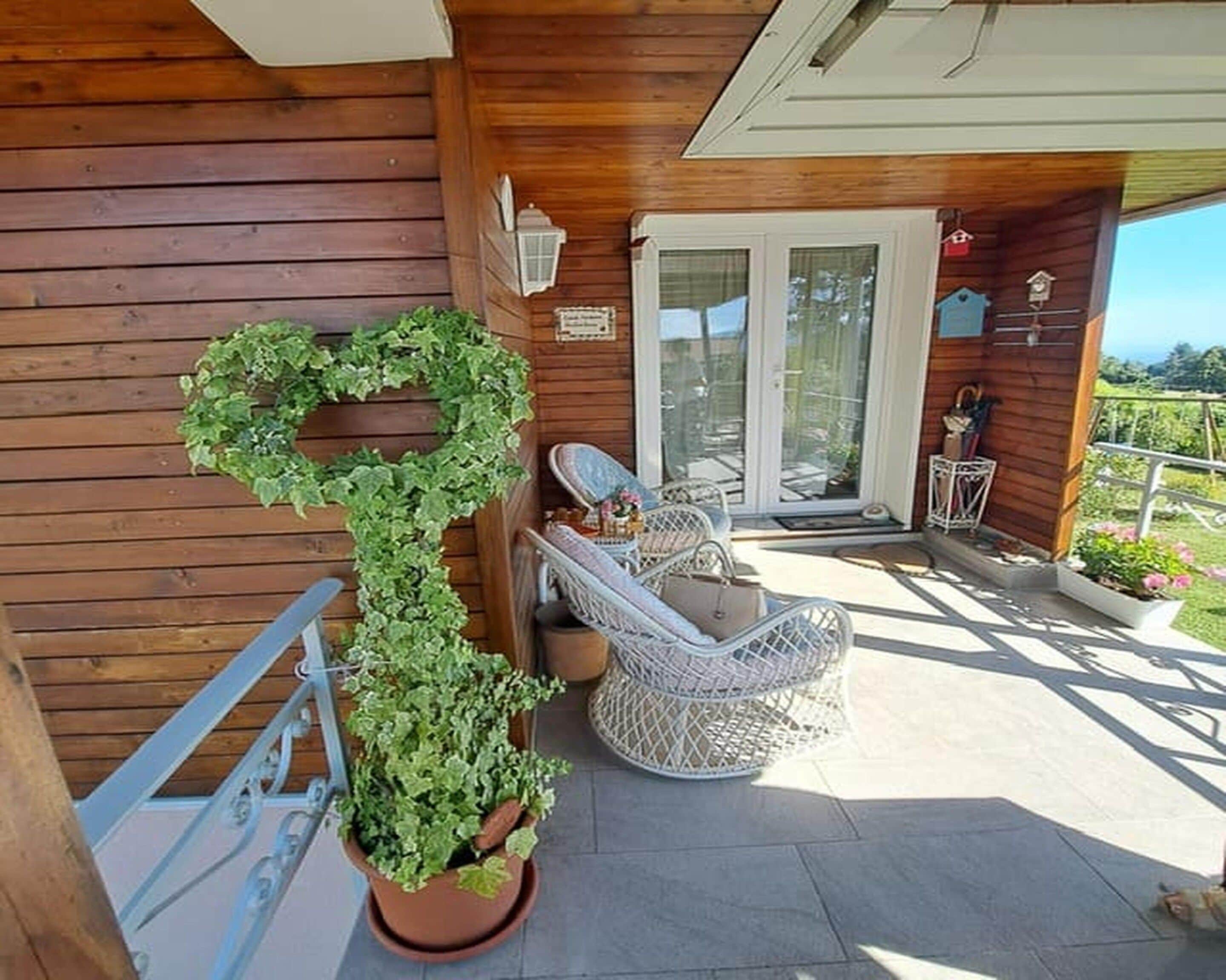 A wooden deck with a potted plant, a wicker chair, and a glass door leading to a covered area.