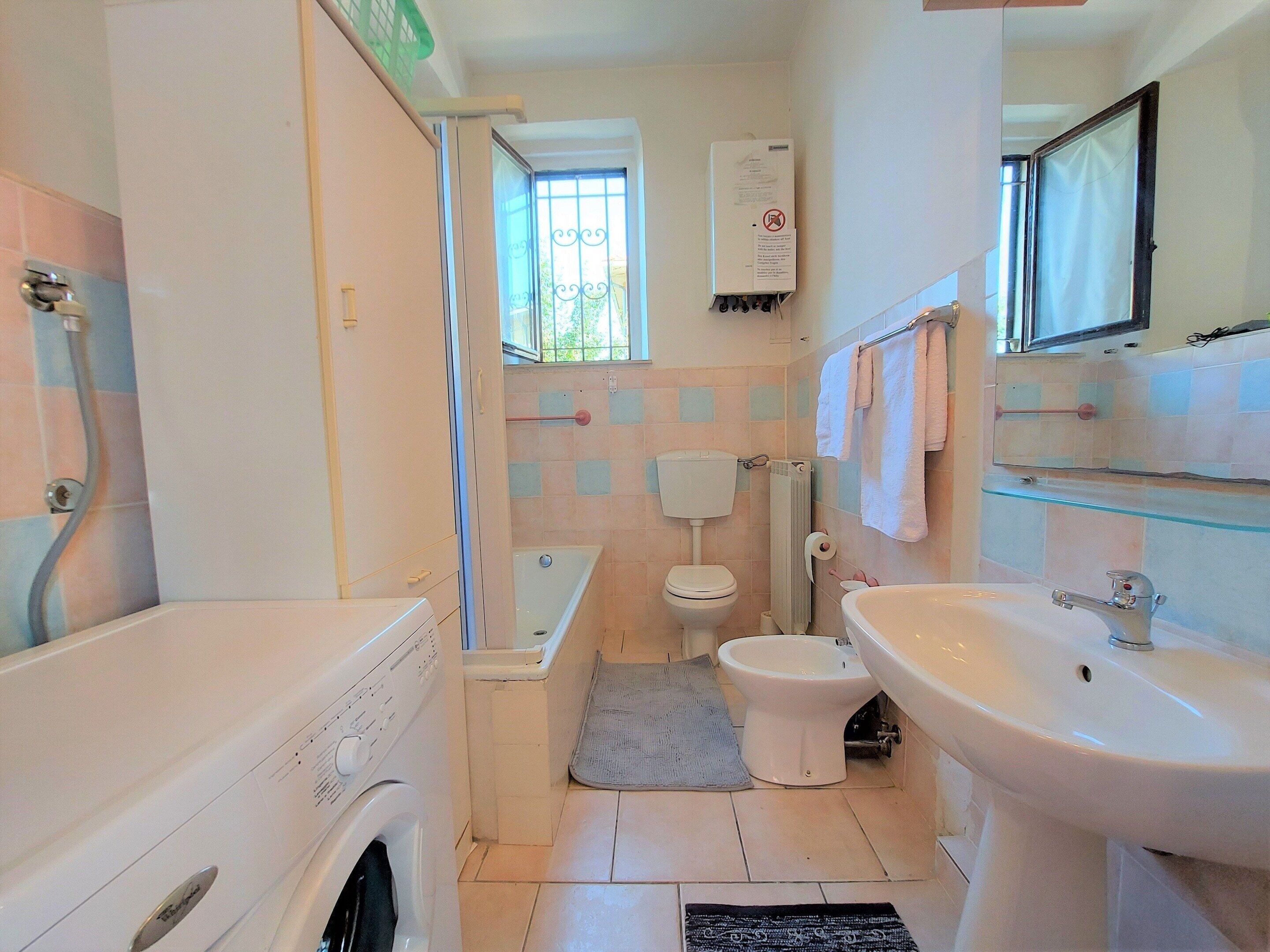 A compact bathroom with a washing machine, a toilet, a bathtub, and a sink.