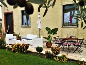 An outdoor seating area with white wicker furniture, a potted plant, and a table with chairs. - Villa in Italy With Private Garden Retreat (Lucignano)